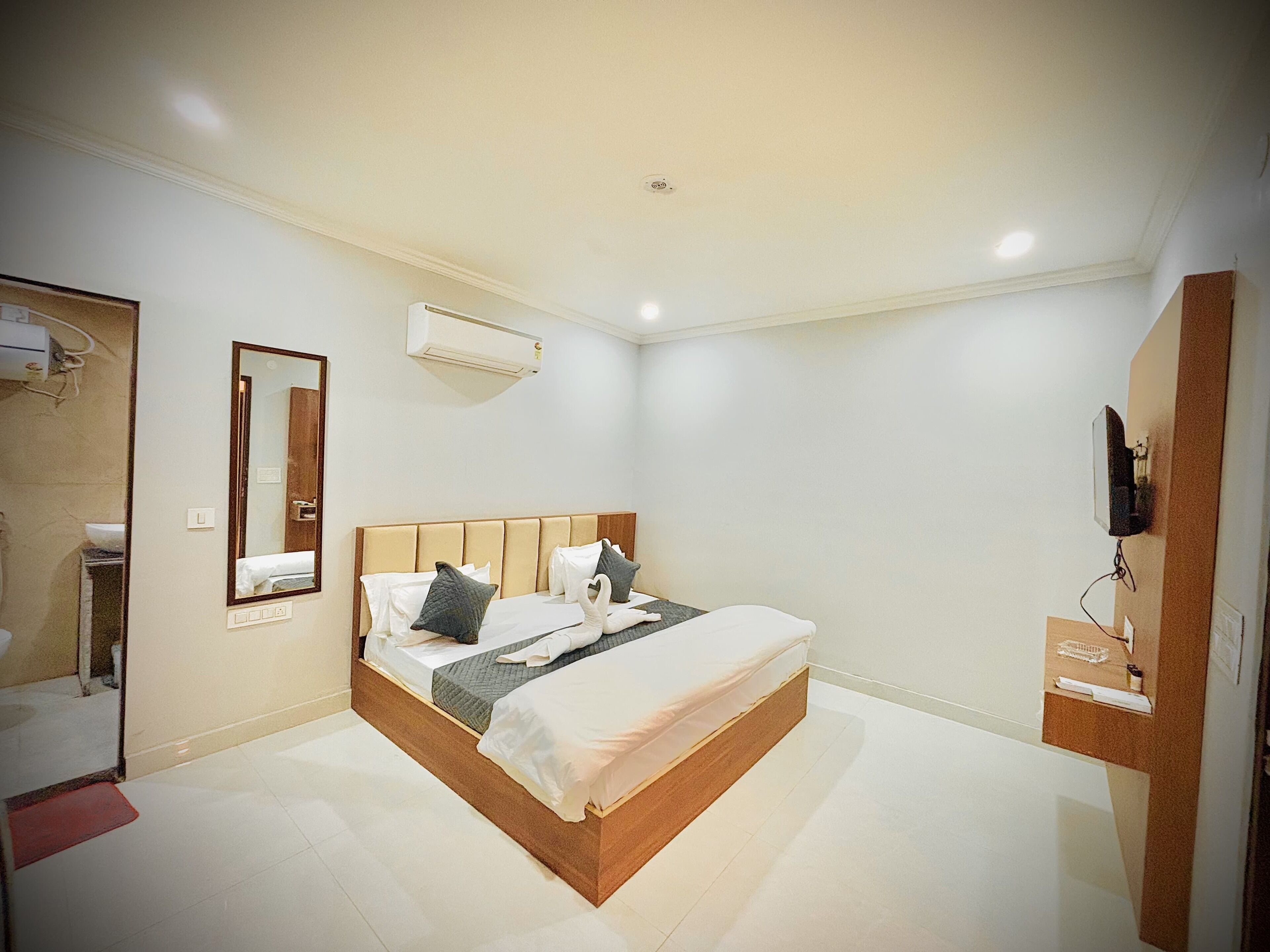 A modern bedroom with a large bed, a built-in air conditioning unit, a mirror, and a mounted television.