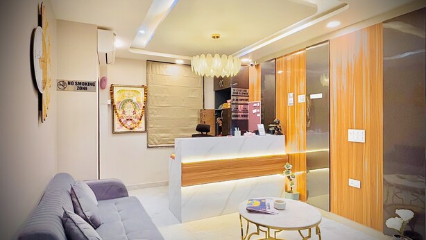 A modern reception area with a sofa, a round gold table, and a counter with a wooden finish. - Hotel Grand Aana Inn (Jaipur)