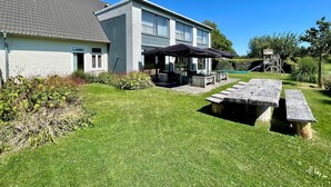 Una casa moderna de dos pisos con un patio que incluye mobiliario exterior y sombrillas.