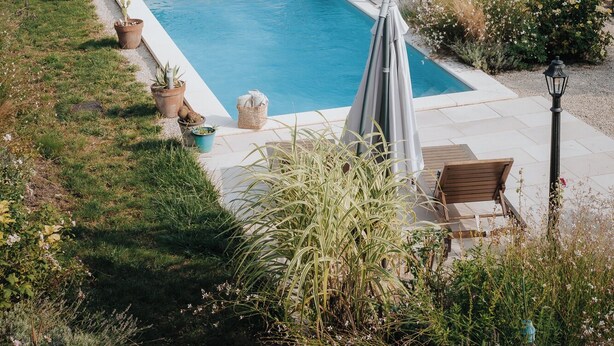Ein Pool mit einer Pergola und Liegestühlen, umgeben von Grünflächen und historischen Steinbauten.