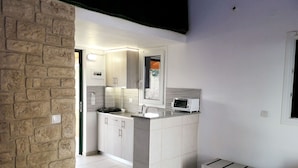 A modern kitchen with white cabinets, a built-in oven, and a microwave. There is a bench and a window in the room. - Cozy studio with Sea View on the beach in Corfu (94X3+83V Kavos, Greece)