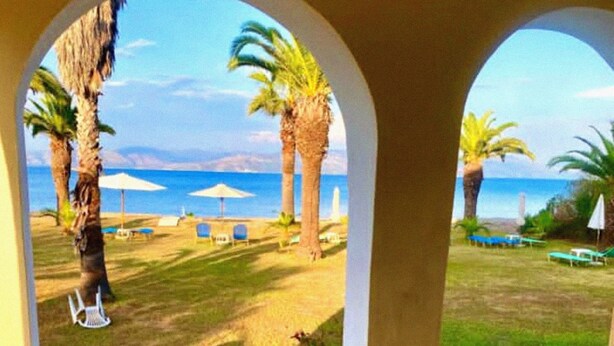 A patio with a view of a beach, palm trees, and lounge chairs. - Cozy studio with Sea View on the beach in Corfu (94X3+83V Kavos, Greece)