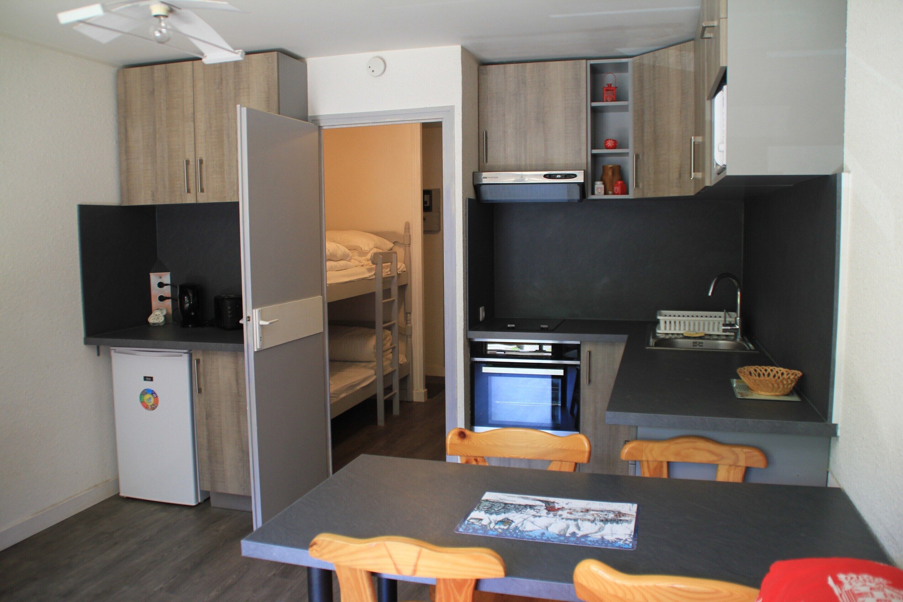 A compact kitchenette with a refrigerator, oven, and microwave. There is a small dining area with a table and chairs.