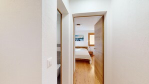 Un couloir étroit mène à une chambre dotée d’un plancher en bois, d’un lit et d’un tableau accroché au mur.