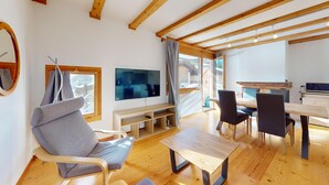 Un salon moderne avec un plafond en bois, un téléviseur fixé au mur, un canapé, une table à manger avec des chaises et un plancher en bois.