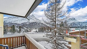 Un balcon offrant une vue sur un paysage montagneux enneigé, comprenant un village et un ciel dégagé.