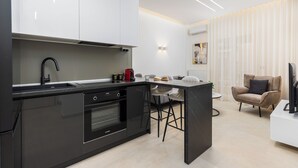 A modern kitchen with black appliances, a dining area with a bar stool, and a living space with a sofa and a TV. - Solange by halu! (Thessaloniki)