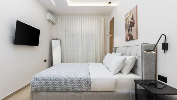 A modern bedroom with a bed, bedside table, and a mounted TV. - Solange by halu! (Thessaloniki)