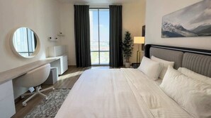Een hotelkamer met een groot bed, een bureau, een stoel, een ronde spiegel, een nachtkastje, een lamp en een schilderij van bergen.
