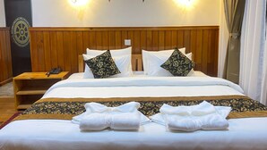 A hotel room with a wooden headboard, a bed with white linens and floral pillows, a bedside table with a phone, and a wall-mounted light fixture. - Hotel Classic Wood (Punakha)
