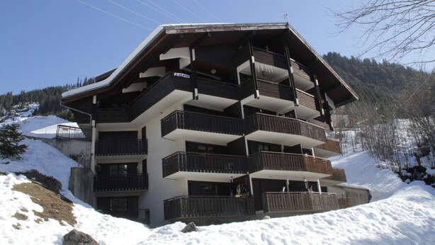 Ein mehrstöckiges Gebäude mit Balkonen in einer verschneiten Berglandschaft.