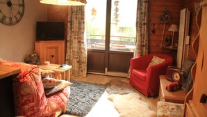 Ein gemütliches Wohnzimmer mit Holzboden, einem roten Sessel, einem Fernseher auf einer Holzkommode und einer großen Uhr an der Wand.