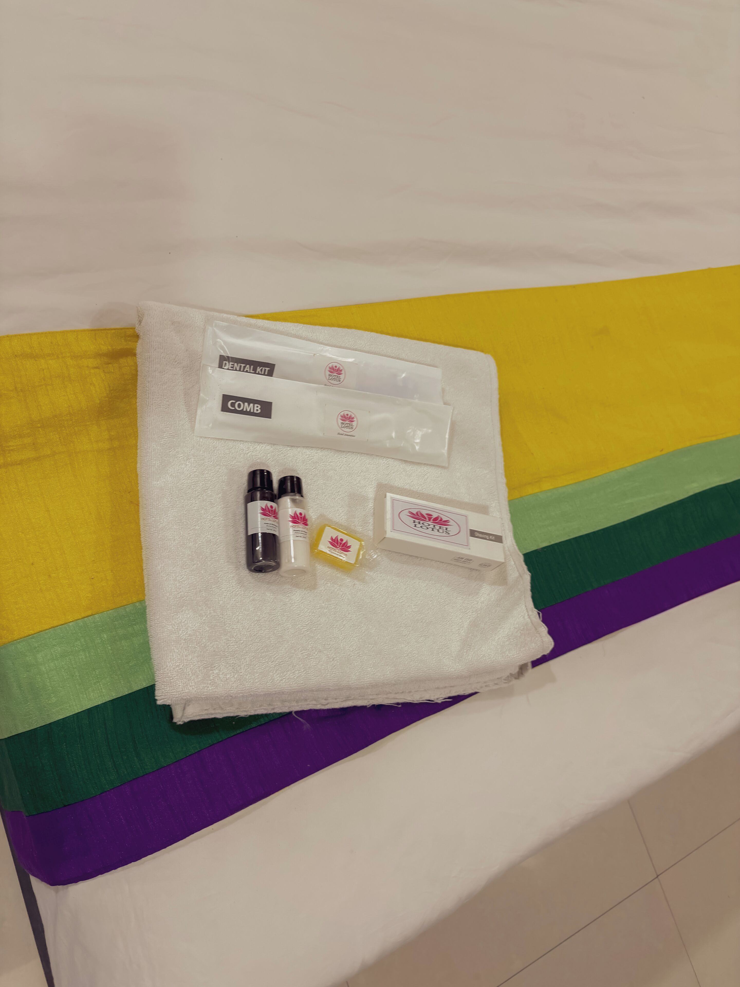 A dental kit and comb on a towel on a bed with a rainbow-striped pillow.
