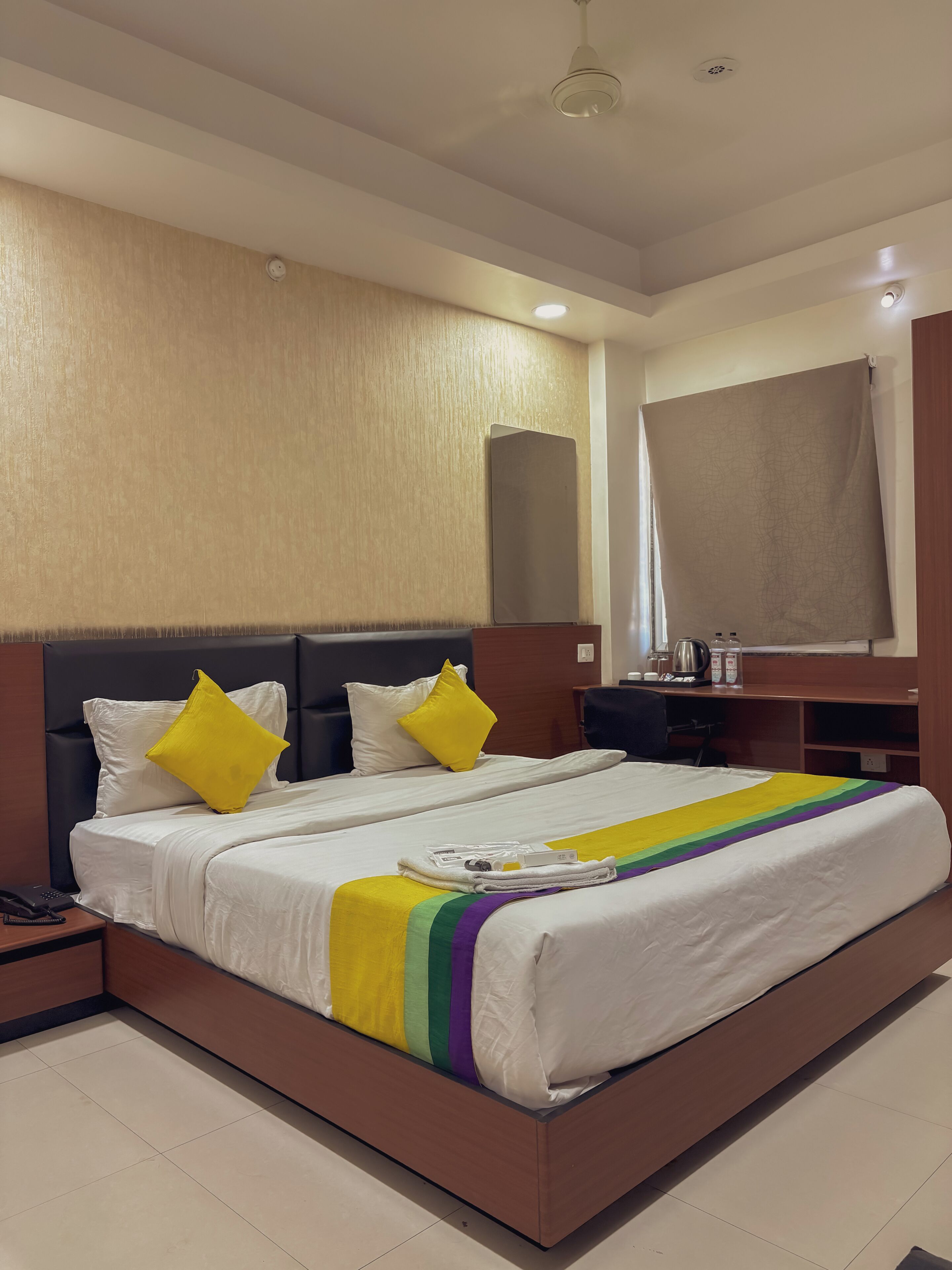 Una habitación de hotel con una cama grande, una mesita de noche, un escritorio y un espejo.