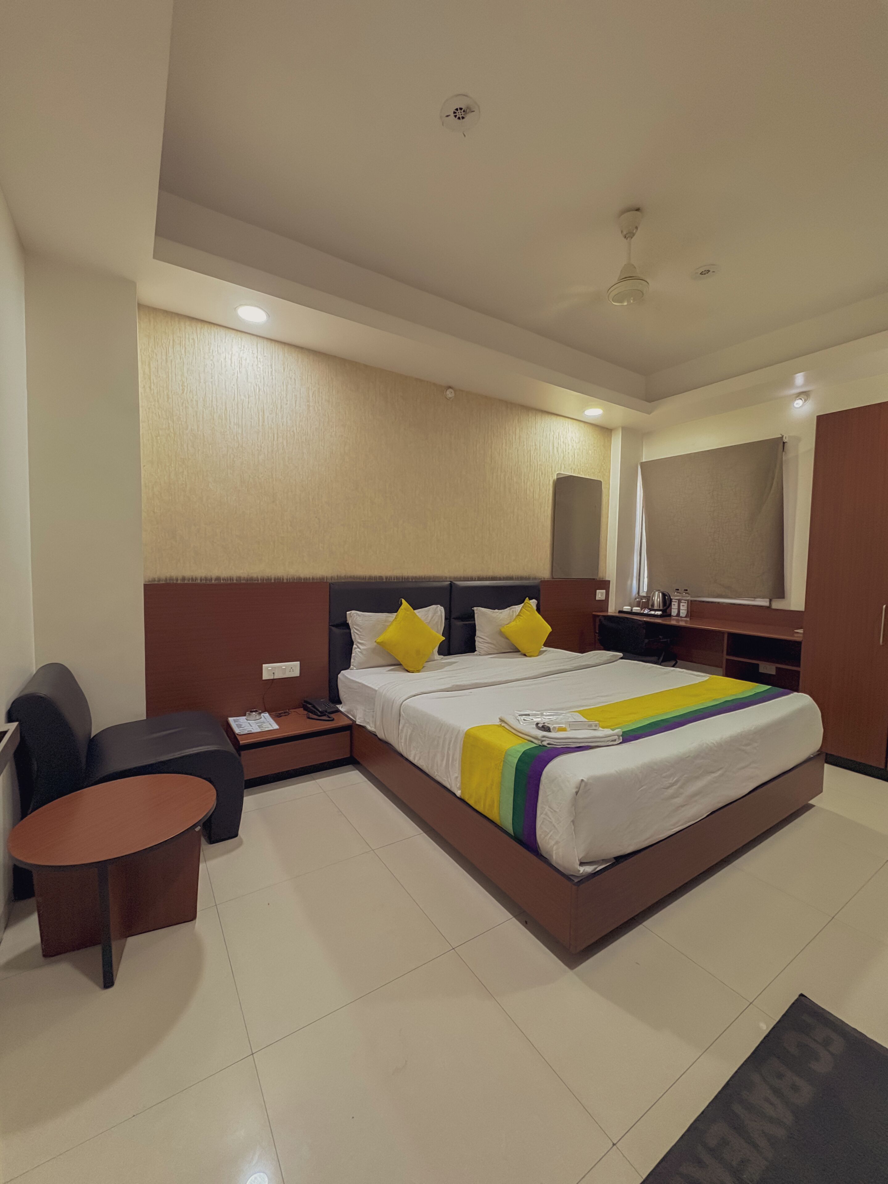 A hotel room with a bed, bedside table, chair, and a small table.