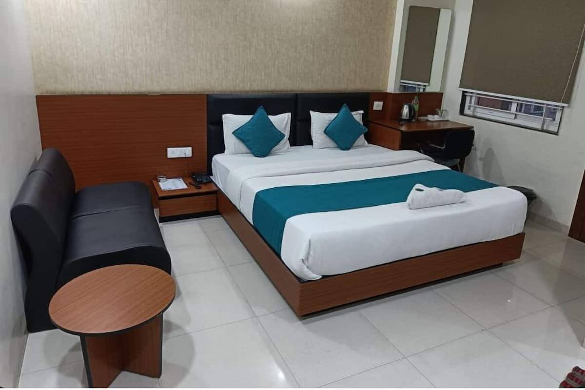 A hotel room with a large bed, a nightstand, a desk, and a sofa.