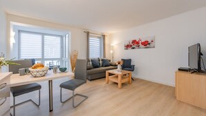 En moderne stue med en sofa, et spisebord med stole, et sofabord og et fjernsyn på et træskab.