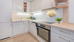 Et moderne køkken med hvide skabe, indbygget ovn og en bordplade med elkedel og en plante.
