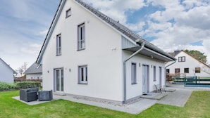 A modern two-story house with a sloped roof, a patio with outdoor furniture, and a well-maintained lawn.