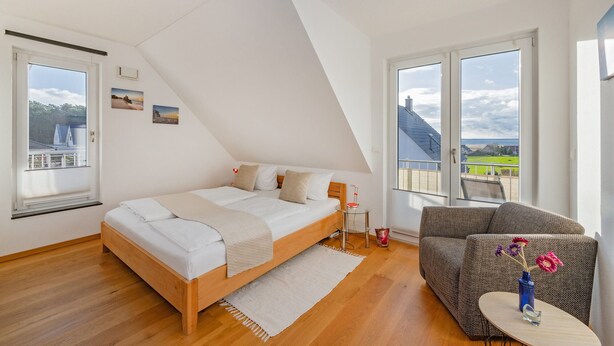 A bedroom with a large bed, a sofa, a small table, and a view of the outside.