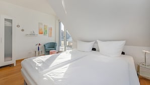 A modern bedroom with a large bed, a small table, a chair, and a window with a view.