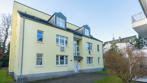 Un immeuble résidentiel de deux étages, doté d’un toit plat, de nombreuses fenêtres et d’un petit jardin à l’avant.