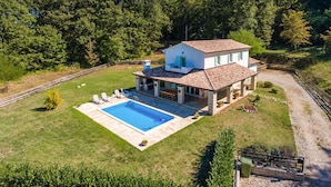 Una casa de dos pisos con piscina, rodeada por un césped cuidado y árboles.