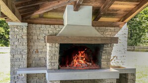 Una chimenea de piedra al aire libre con chimenea, rodeada de muros de piedra y techo de madera.