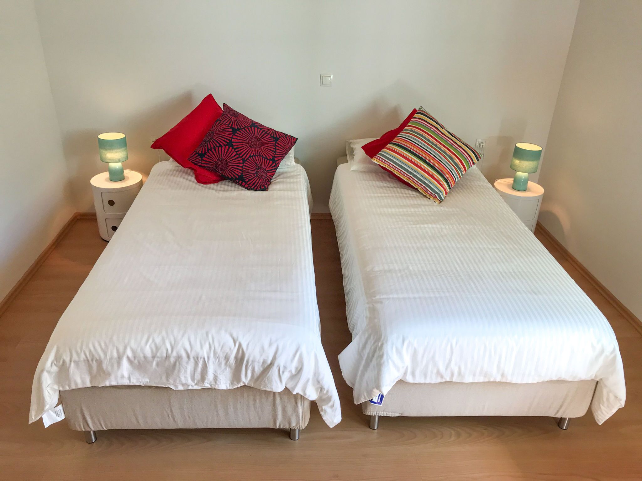 Two single beds with white bedding, red and striped pillows, and bedside lamps.