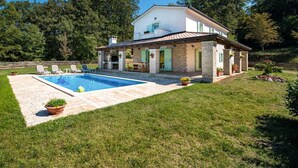 Una casa de dos plantas con piscina, fachada de piedra y césped bien cuidado.