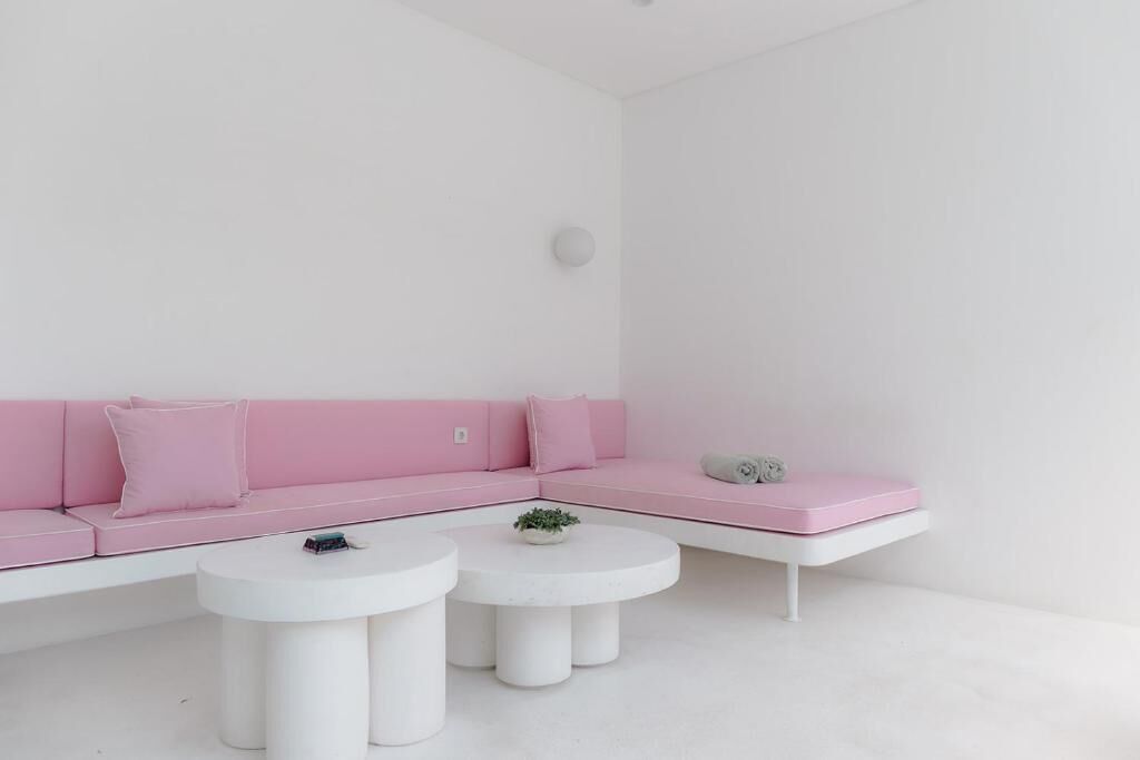 A minimalist room with a pink sofa, two white round tables, and a white ceiling.