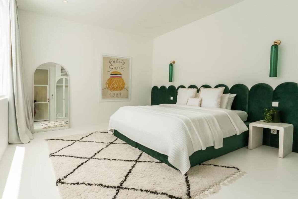 A bedroom with a green upholstered headboard, a white bedspread, a white rug, and a framed picture on the wall.