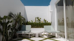 Un patio extérieur moderne, doté de deux fauteuils et d’une table ronde, et agr émenté de différents cactus et plantes.