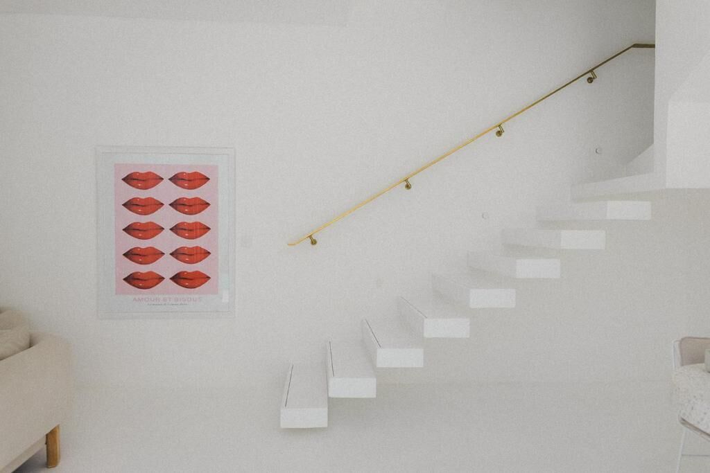 A staircase with a wooden handrail and white steps, a framed artwork of red lips, and a beige sofa in a minimalist room.