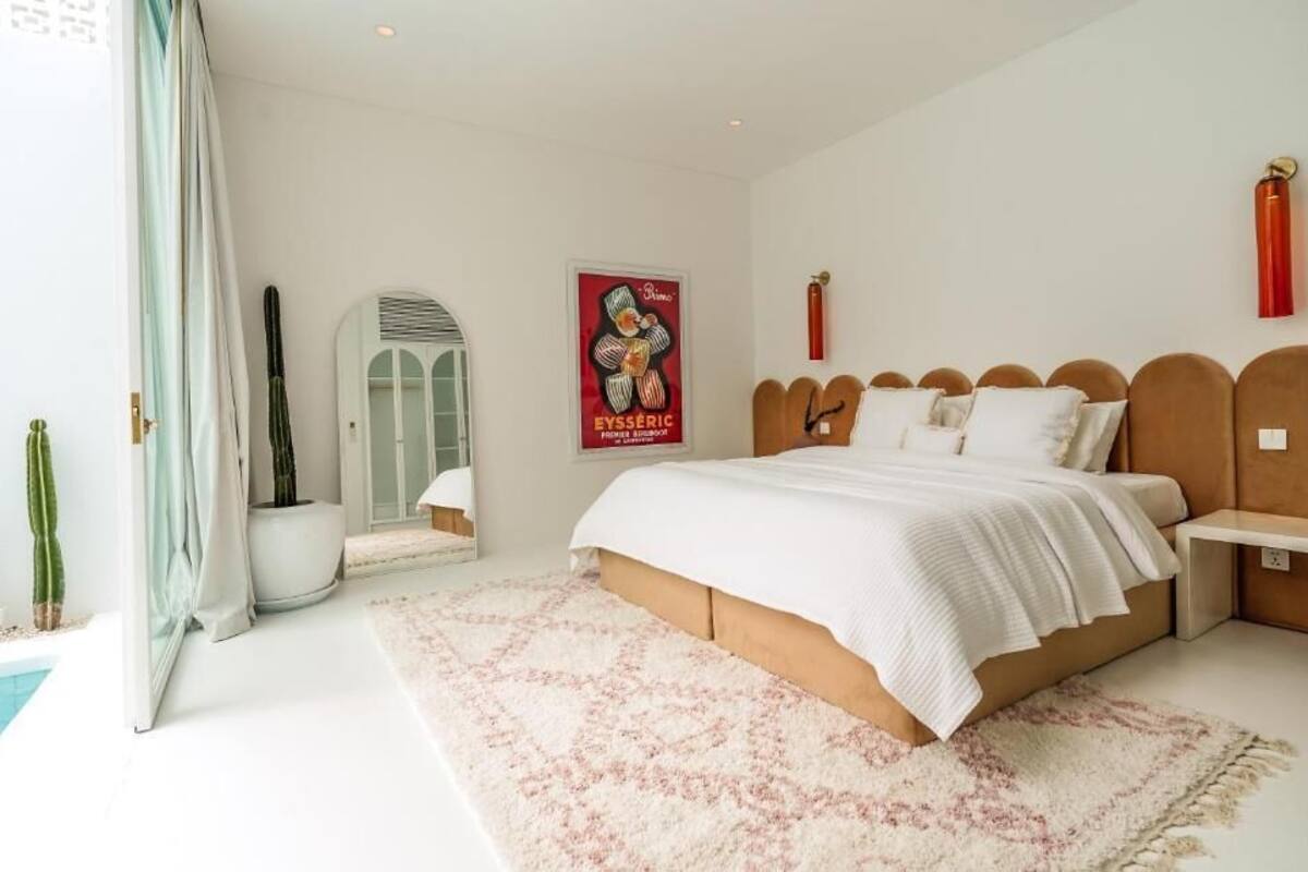 A bedroom with a bed, bedside tables, a nightstand, a poster, a window with curtains, and a potted plant.