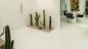 Un intérieur moderne au design minimaliste, comprenant un coin repas avec une table et des chaises blanches, un petit jardin de cactus et une grande verrière.
