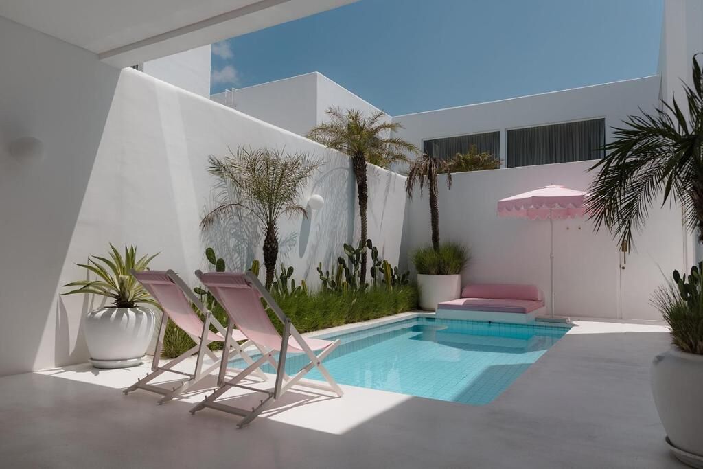 Un espace piscine extérieur moderne, doté de deux chaises longues, d’un petit coin salon et d’une plante en pot.