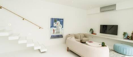 Una sala moderna con un sofá blanco, un reposapiés azul y una escalera con escalones blancos.