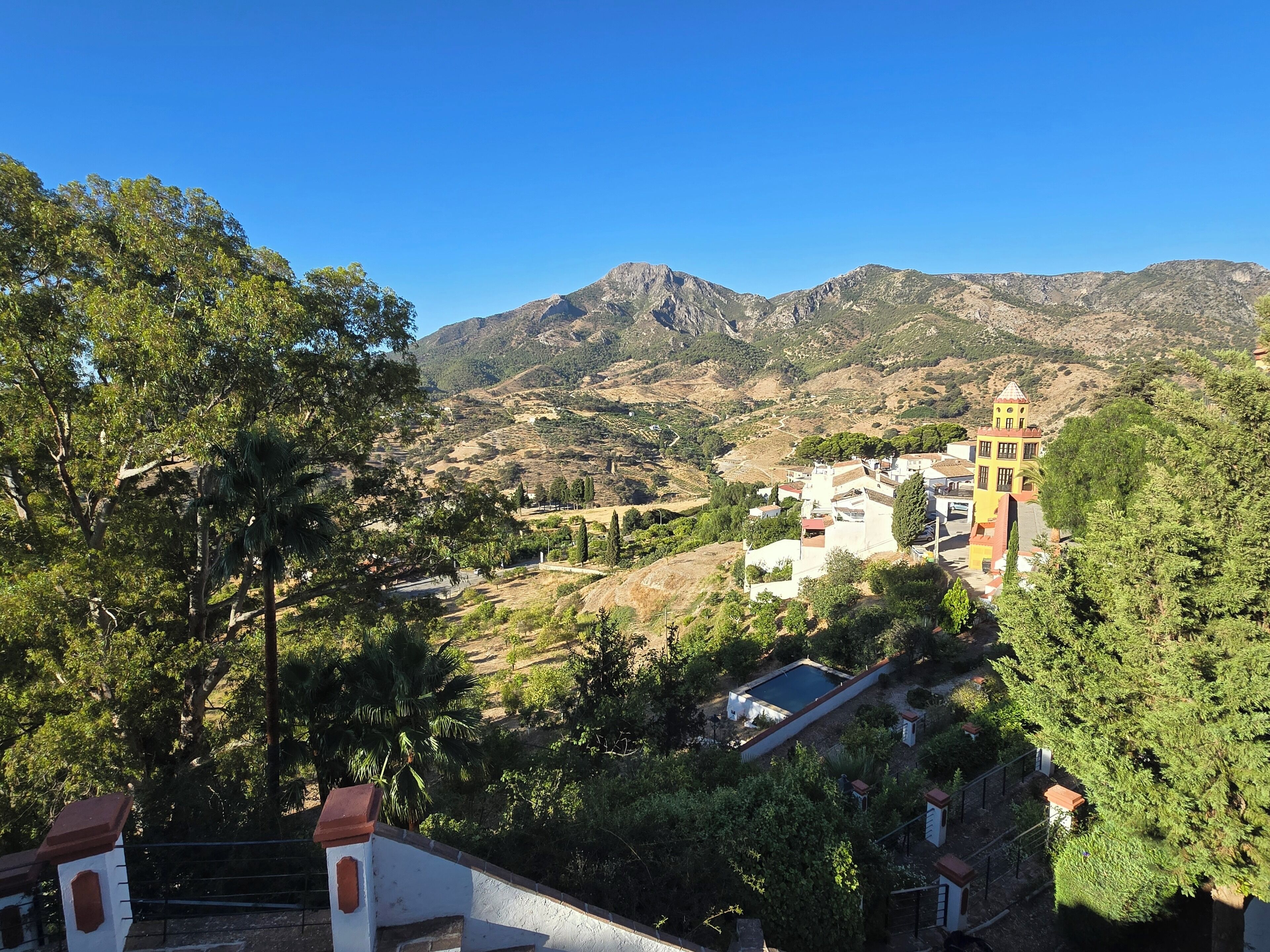 Paisaje montañoso con un pueblo, incluyendo una torre amarilla destacada.