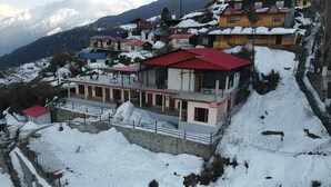 A snow-covered building with a red roof, surrounded by snow-covered hills and mountains. - Pine Palace Homestay (Joshimath)