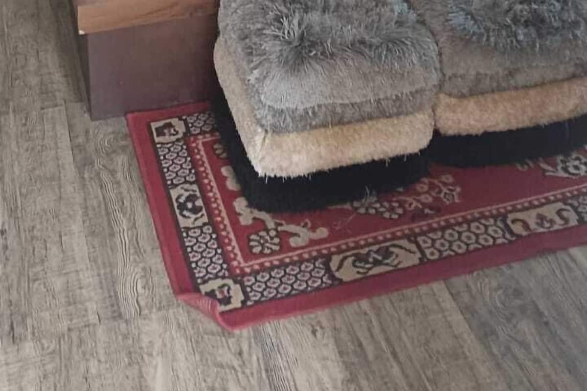 Una cama con cabecera blanca, almohadas rojas y blancas, una colcha con estampado de coches y un reposapiés gris y mullido.