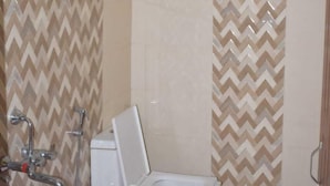 A bathroom with a toilet, shower, and a red bucket. - Pine Palace Homestay (Joshimath)