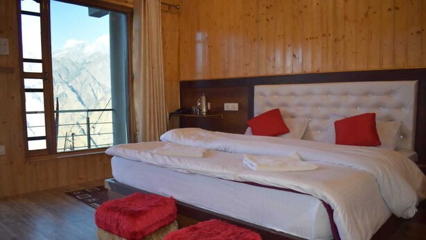 A bedroom with a large bed, wooden walls, and a view of mountains through a window. - Pine Palace Homestay (Joshimath)