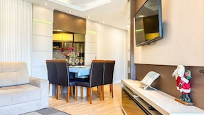 Un salon moderne comprenant un coin repas, un téléviseur à écran plat fixé au mur et une petite table sur laquelle est posée une figurine du Père Noël.