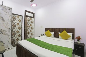 A neatly arranged hotel room with a bed, a nightstand, a chair, and a wardrobe. - Twamev Residency (New Delhi)