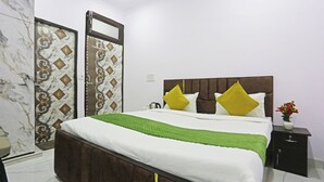A neatly made bed with a green bedspread and two yellow pillows, a nightstand with a vase of flowers, and a marble-patterned wall. - Twamev Residency  (New Delhi)