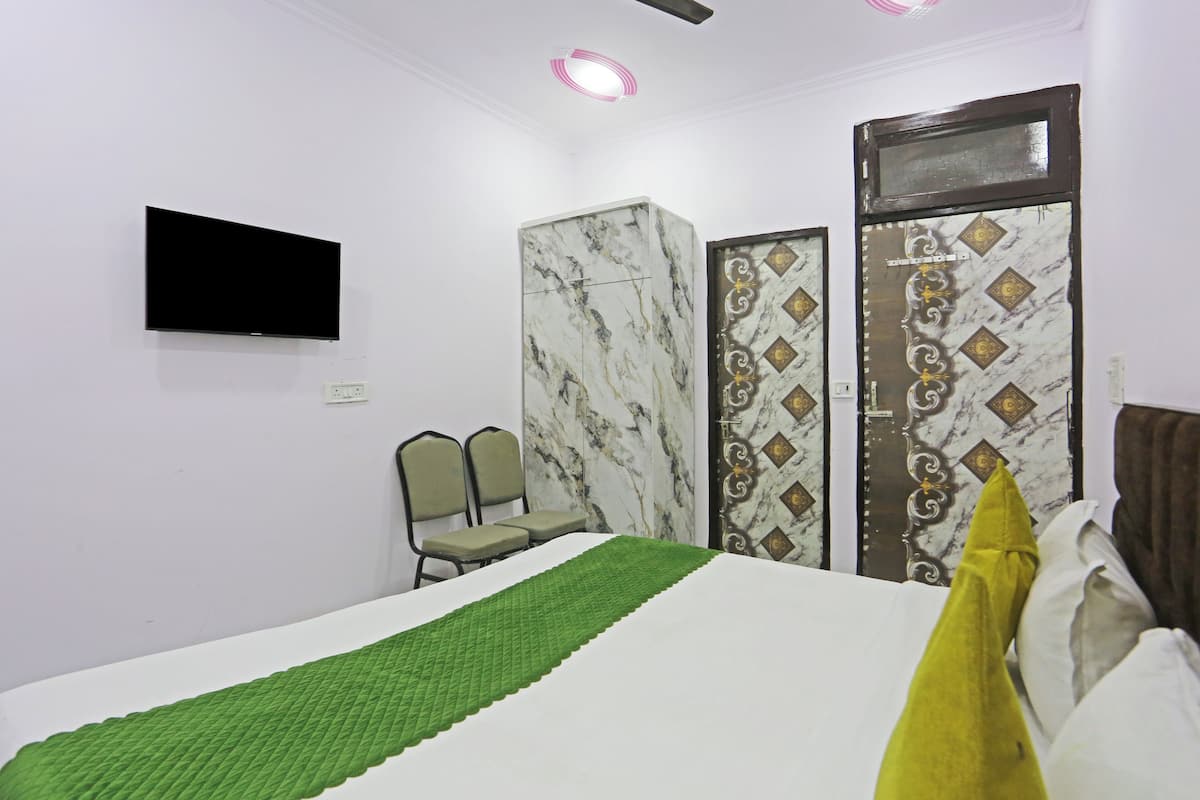 A hotel room with a bed, a flat-screen TV mounted on the wall, a green bedspread, two chairs, and a decorative door.