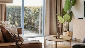 A modern living room with a sofa, a round coffee table, and a large window overlooking a garden.