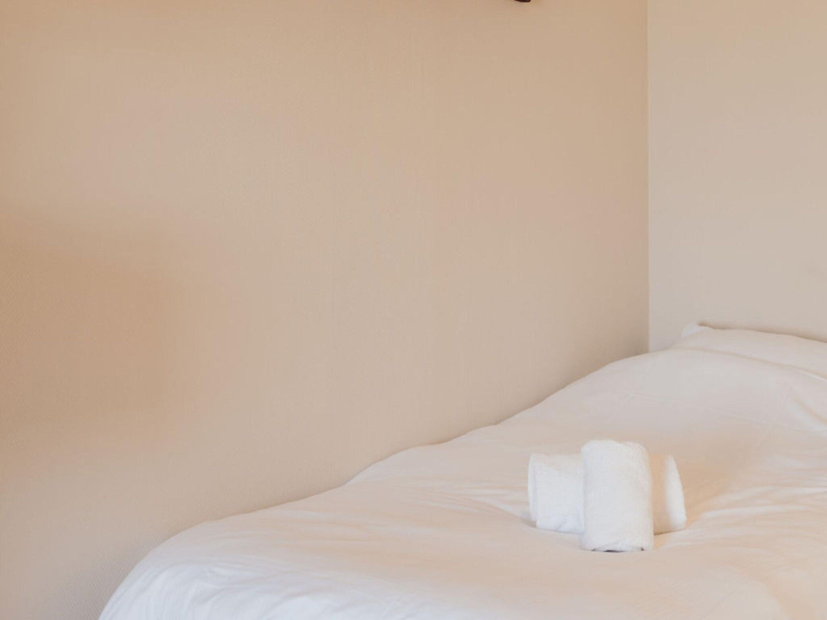 Una cama bien hecha con sábanas blancas y dos toallas enrolladas al pie.