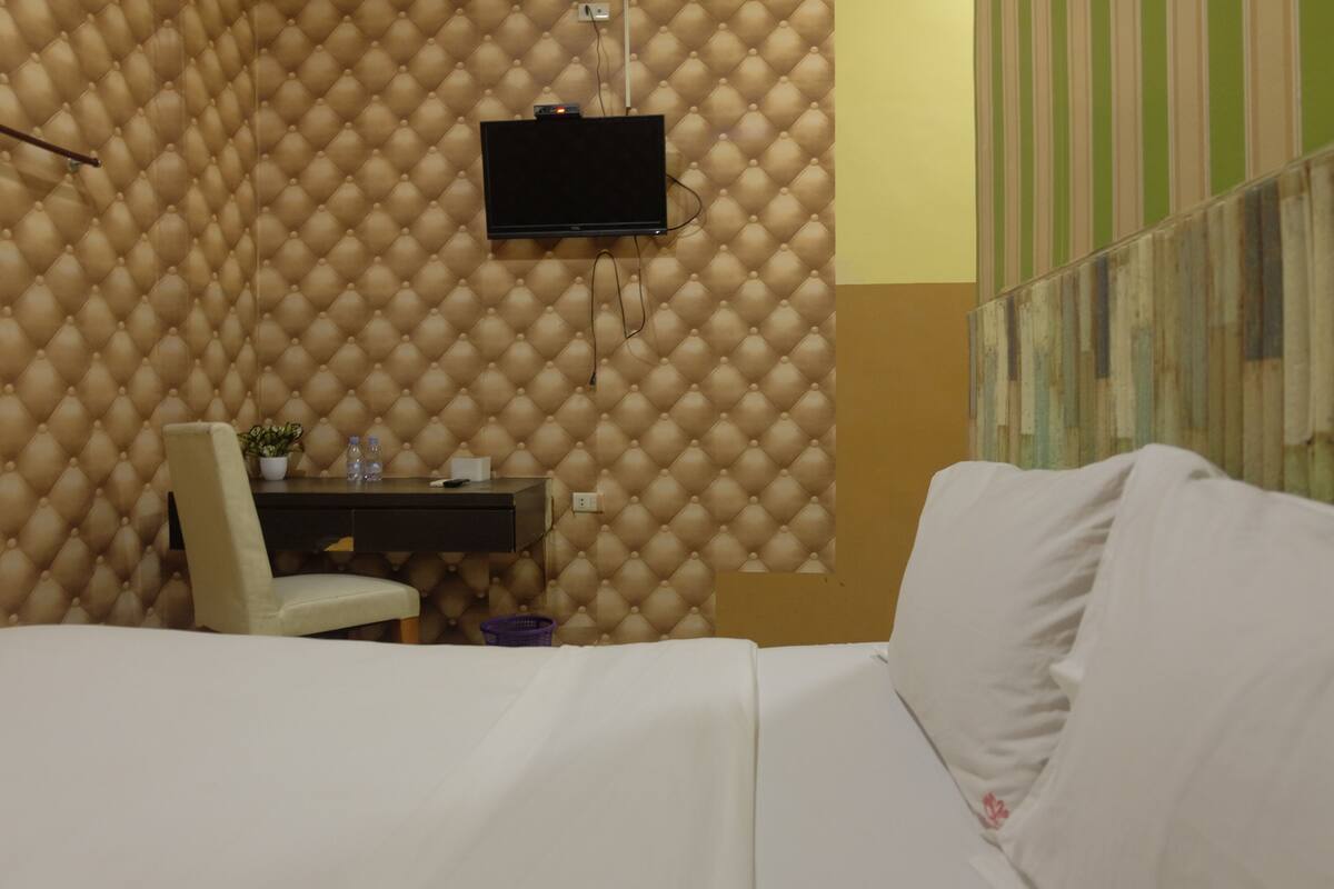 Ein Hotelzimmer mit Bett, Schreibtisch mit Stuhl, Wandfernseher und einem Streifenmuster-Vorhang.